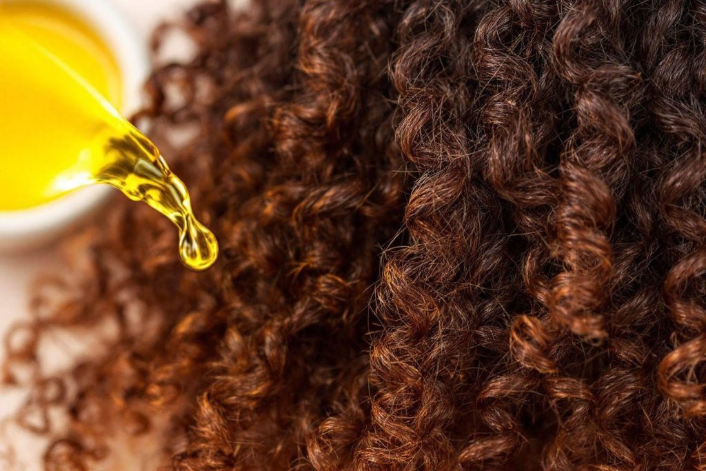 Huile capillaire appliquée sur des cheveux bouclés