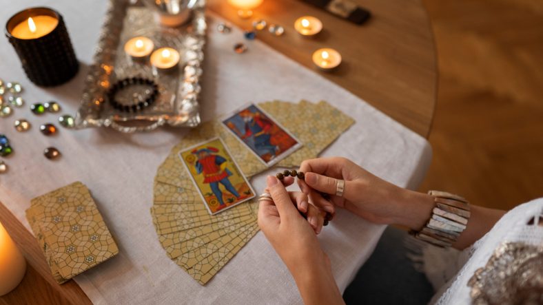 Personne réalisant un tirage de tarot dans une ambiance éclairée aux bougies
